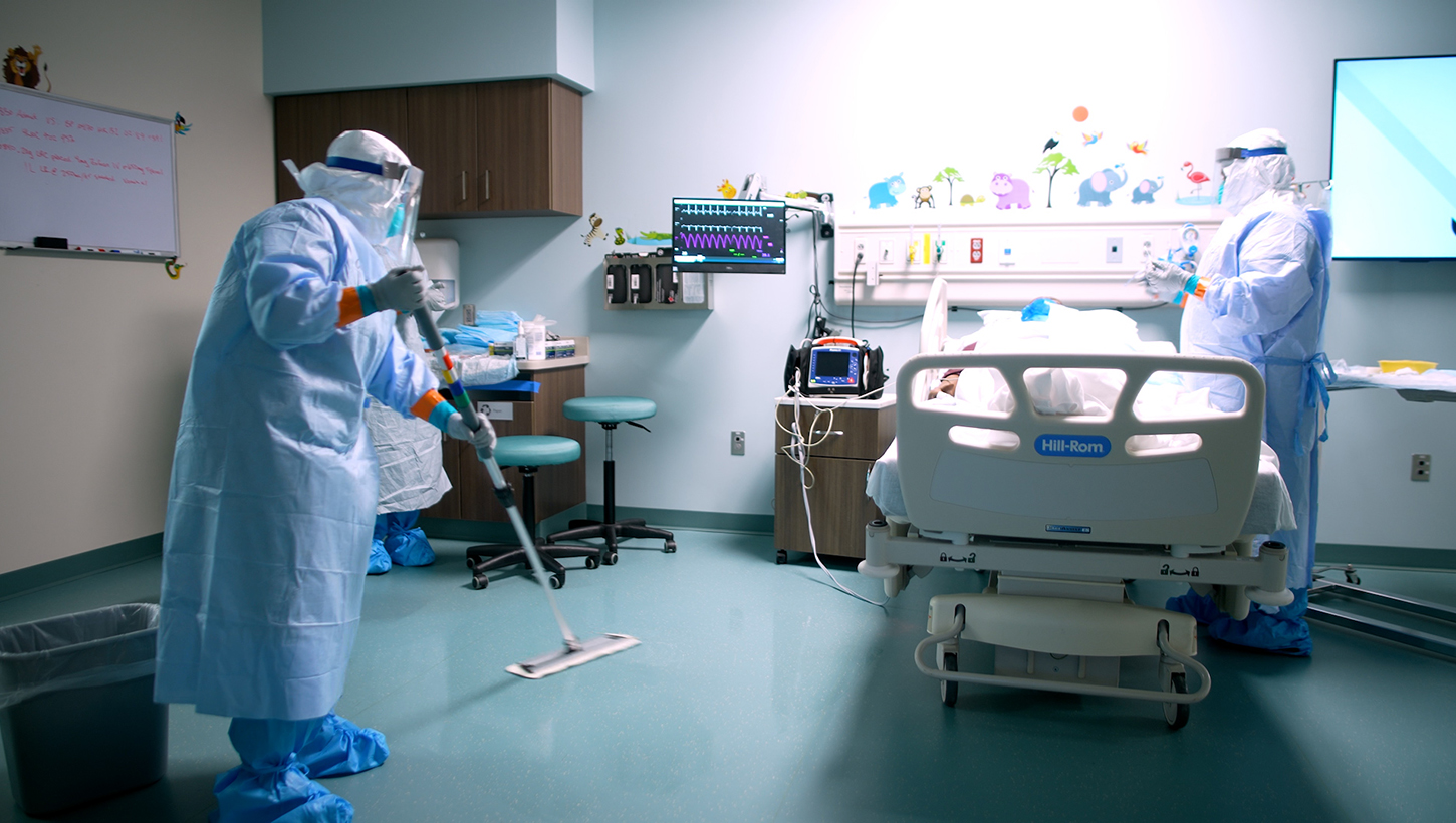 A medical professional from the Center for Sustainment of Trauma and Readiness Skills (C-STARS) Omaha, in full personal protective equipment, mops the floor while another team member tends to a simulated patient