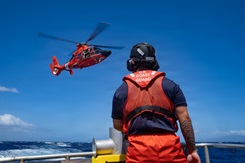 Photo by Petty Officer 3rd Class Avery Tibbets, U.S. Coast Guard Oceania: A Coast Guard crew member assigned to Coast Guard Station Maui in Maalaea, HI, observes an MH-65 Dolphin helicopter from the back of a 45-foot Response Boat-Medium. This work must comply with the restrictions shown on https://www.dvidshub.net/about/copyright