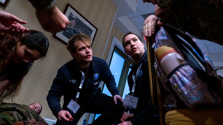 Civilian pre-med students and military personnel collaborate during a simulated high-stress medical intervention. 