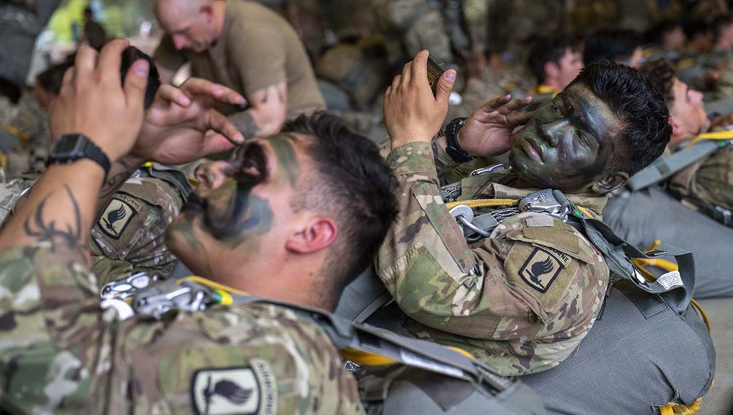 Army paratroopers, assigned to the 173rd Airborne Brigade, apply camouflage paint to their faces while they wait to board an aircraft