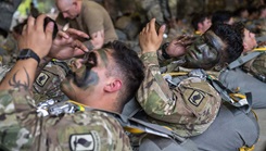 Army paratroopers, assigned to the 173rd Airborne Brigade, apply camouflage paint to their faces while they wait to board an aircraft