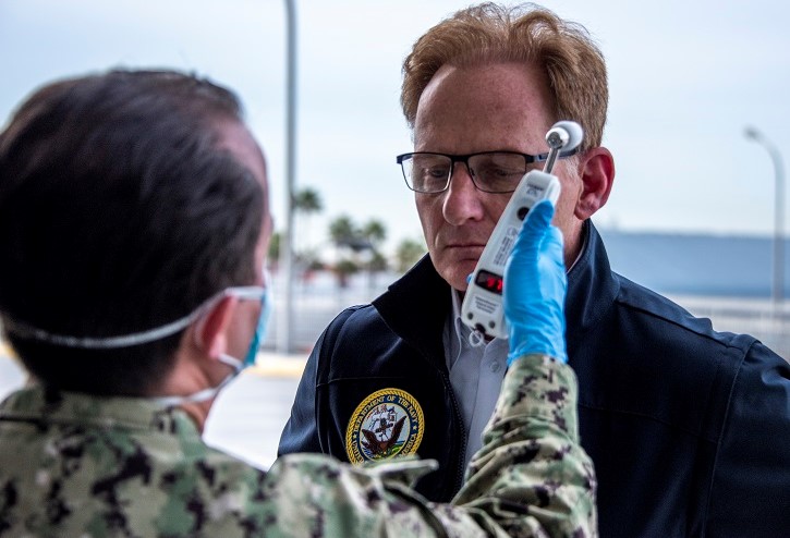 Image of man getting his temperature taken by service member wearing a mask.