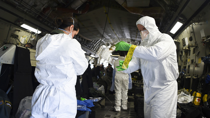 Airmen assist one another in donning their personal protective equipment, while on-board an Air Force C-17 Globemaster III during transportation isolation system training at Joint Base Charleston, South Carolina. Engineered and implemented after the Ebola virus outbreak in 2014, the TIS is an enclosure the Department of Defense can use to safely transport patients with diseases like novel coronavirus. (U.S. Air Force photo by Senior Airman Cody R. Miller)