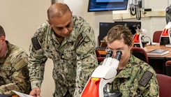 A U.S. Navy officer reviews lab materials with a student as she examines specimen slides under a microscope. 