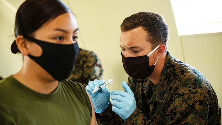 Image of Healthcare worker giving vaccine to soldier; both wearing masks.