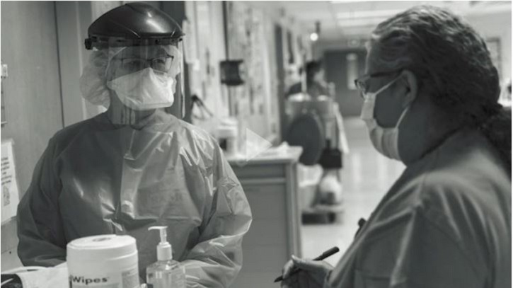 Link to Video: Black and white image of two nurses wearing PPE in a hospital setting