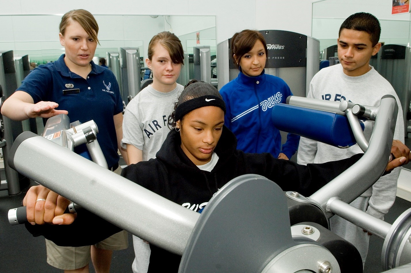 four teenagers with air force attire work on an exercise machine with an adult trainer