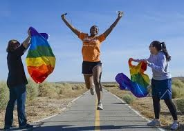 Runner on road jumping between two spectators waving rainbow flags